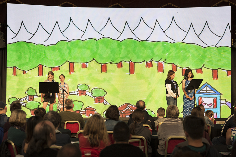 Pupils read on stage with their artwork projected behind them at the Edinburgh International Book Festival