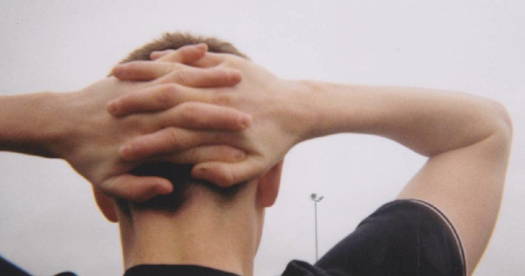 A boy's hands are clasped behind his head and he faces away from the camera