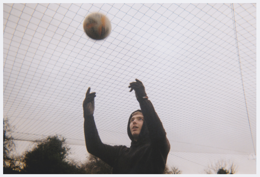 A teenage boy wearing a black hoodie and black gloves is throwing a football into the air